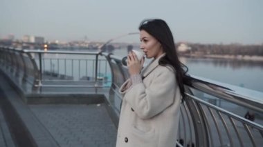 Elinde kahve olan genç kız iş merkezinin yanındaki caddede duruyor. İş kadını sıcak, canlandırıcı bir içki içer.