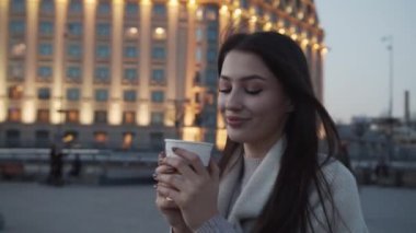 Gece Kiev 'de uzun saçlı çekici esmer kız elinde bir fincan kahve ya da çayla yürüyor.