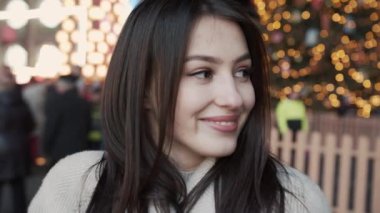 Çekici bir esmer, büyüleyici bir gülümsemesi var Noel pazarında duruyor ve kameraya bakıyor. Yeni yıl. Yeni yıl tatili. Yeni yıl hediyeleri..