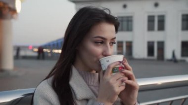 Elinde bir fincan kahve olan bir kadın. Siyah saçlı esmer kız, şehir sokaklarında kahve içiyor. Sıradan sokak modası.
