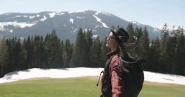 Kafkasyalı bir kadının, saçlarında ağaçlar ve dağlardan oluşan bir arka planda rüzgarın esmesiyle çayırda neşeli bir şekilde yürüdüğü yakın plan görüntüsü. Mutluyum. Güneşli bir gün.