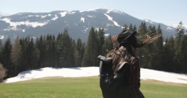 Yavaş çekim, kafkasyalı bir kadının şapkasını çıkarmış çayırda neşeyle yürüdüğü ve saçlarının arasından ağaçlar ve dağlardan oluşan bir zemine doğru esen rüzgarın görüntüsü. Mutluyum. Güneşli