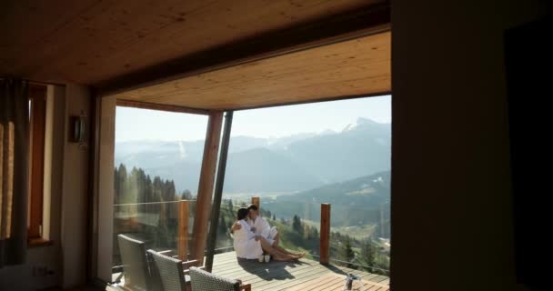 Imágenes en cámara lenta de una pareja feliz en una escapada de luna de miel besándose en el balcón de su cabaña de montaña. — Vídeos de Stock