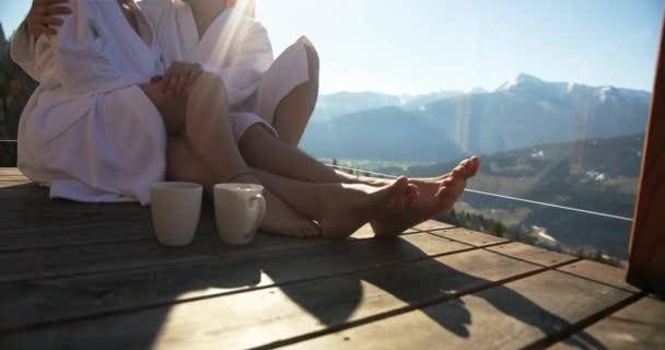 Tett inntil, sakte film av et kaukasisk par som sitter og kjærtegner hverandre kjærlig på balkongen i hytten. Nydelig fjellutsikt. Romantisk flukt. – stockvideo