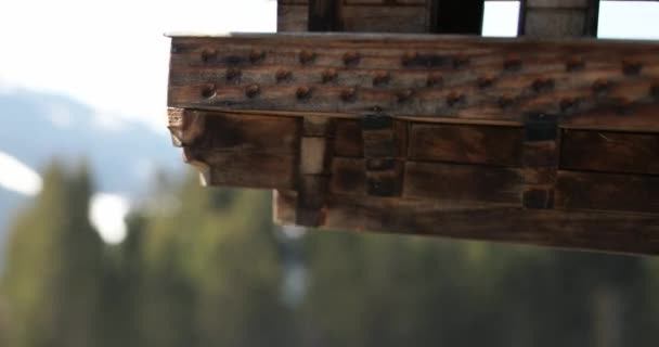 Super close-up of footage of a small wooden-house artefact hanging from a thread and swinging slowly against a blurred background of trees and mountains. outdoors. Nature. — Stock Video