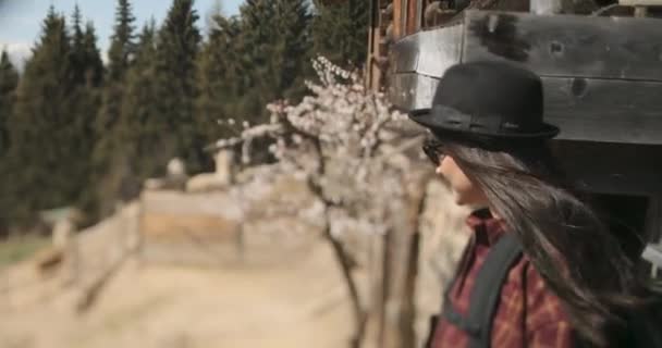 Boční profil brunetky, která stojí před svým domem s kloboukem a dívá se na své lamy. — Stock video