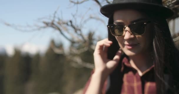 Imágenes de cerca de una hermosa mujer caucásica con un sombrero negro y gafas de sol en un día soleado. — Vídeos de Stock