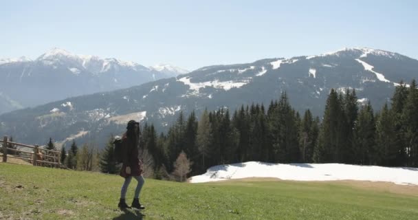 Amplio plano de una hembra irreconocible caminando por un prado y disfrutando de la vista de los árboles y montañas alrededor en un día soleado. — Vídeos de Stock