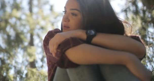 Close-up, backlit footage of a sad, young, beautiful brunette female thinking deep with her arms wrapped around her folded legs. — Stok Video