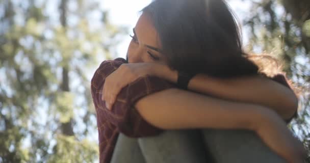 Close-up, verlichte beelden van een trieste, jonge, mooie brunette vrouw die diep nadenkt met haar armen om haar gevouwen benen. — Stockvideo
