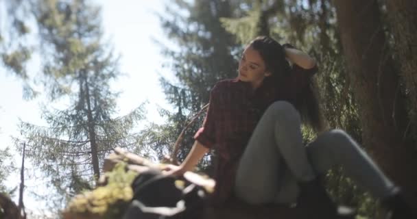 Nære bilder av en vakker, ung brunette kvinne som tenker mens hun sitter på en stor tømmerstokk i skogen. – stockvideo