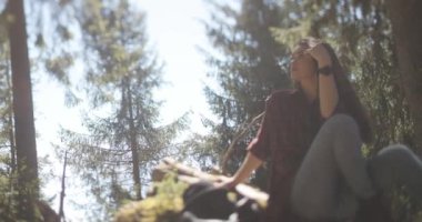 Güzel, genç, esmer bir kadının, parmaklarını saçlarında gezdirip derin derin düşünürken, ormanda büyük bir kütüğün üzerinde otururken çekilmiş yakın çekim görüntüleri..