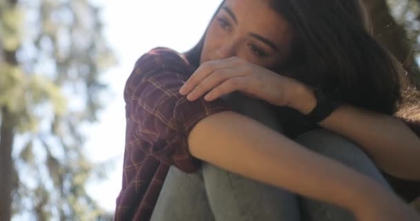 Close-up, verlichte beelden van een trieste, jonge, mooie brunette vrouw die diep nadenkt met haar armen om haar gevouwen benen. — Stockvideo