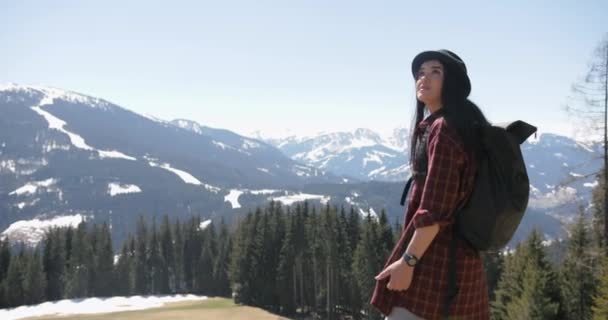 Imagens de uma mulher morena usando um chapéu observando uma bela vista de montanhas e árvores, ela verifica seu tempo e se afasta. — Vídeo de Stock