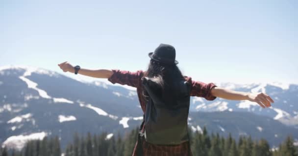 Rear melihat rekaman dari seorang wanita berambut cokelat riang mengenakan topi mengamati pemandangan indah gunung-gunung dan pohon dengan tangannya membentang luas saat ia menikmati angin sejuk udara segar. — Stok Video