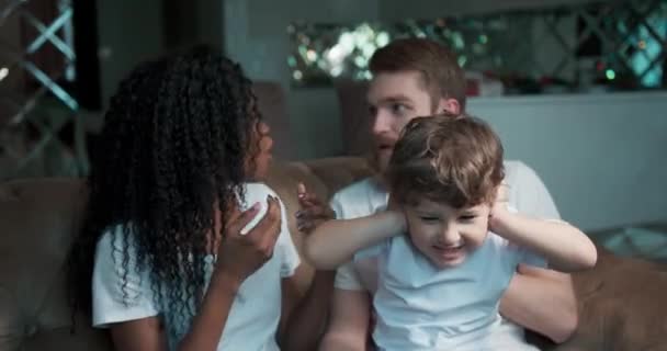 Сумний і роздратований маленький хлопчик блокує шум від батьків, які борються вдома у вітальні . — стокове відео
