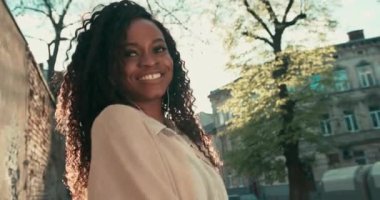 Güzel, mutlu, kıvırcık saçlı ve kameraya cilveli bakışlı Afro-Amerikan bir kadının yakın plan portresi. Güneşli bir günde dışarıda eğlenmek..