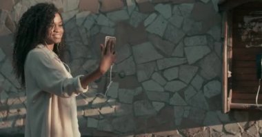 Sokakta yürüyen ve akıllı telefonuyla selfie çeken muhteşem bir Afro-Amerikalı kadının yan görüntüsü. Dışarıda eğlenmek için.