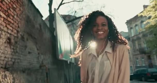 Vista retroilluminata di una bella donna afro-americana felice con ricci che saltano e si girano per guardare la telecamera. Divertimento all'aria aperta in una giornata di sole. — Video Stock