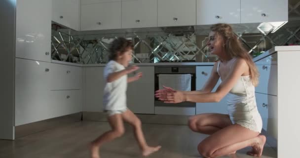 Filmagem de uma mãe se ajoelhando para levantar o filho e abraçá-lo enquanto ele corre para a cozinha. — Vídeo de Stock