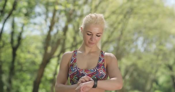 Nahaufnahme einer schönen kaukasischen Blondine, die auf ihre Uhr schaut und im Park weiterjoggt. Ausdauertraining. — Stockvideo