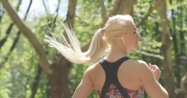 Yakın çekimde, parkta müzik dinlerken koşan sarışın bir fitness kadınının yavaş çekim görüntüleri. Saçları sağa sola sallanıyor..