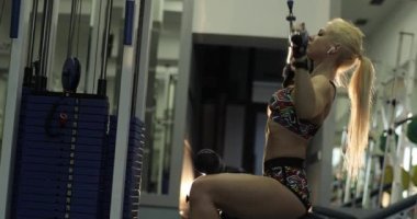 Yakından, yavaş çekimde, spor salonundaki yoğun kardiyo egzersizi sırasında, at kuyruklu genç sarışın bir bayanın bariyeri indirirkenki görüntüsü..