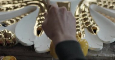 Bir el kamerasının yakın plan çekimleri, arka planda sarı boya bulunan bir ev süsünü dikkatlice özelleştiriyor.