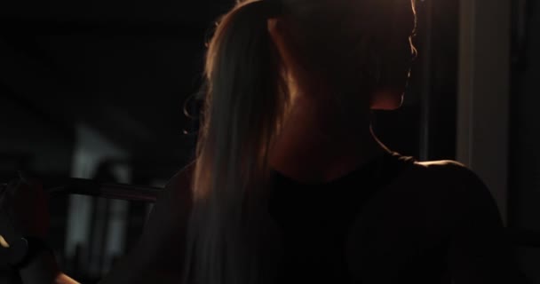 Super close-up, backlit tampilan belakang seorang wanita kebugaran menarik ke bawah bar pada mesin lat. Rutinitas latihan kardio. — Stok Video