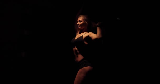 Attractive blonde female flaunting her perfectly toned body in a black background. — Stock Video