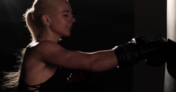 Imágenes de vista lateral de cerca de una determinada boxeadora rubia golpeando agresivamente golpes en una bolsa de boxeo durante el entrenamiento. — Vídeos de Stock