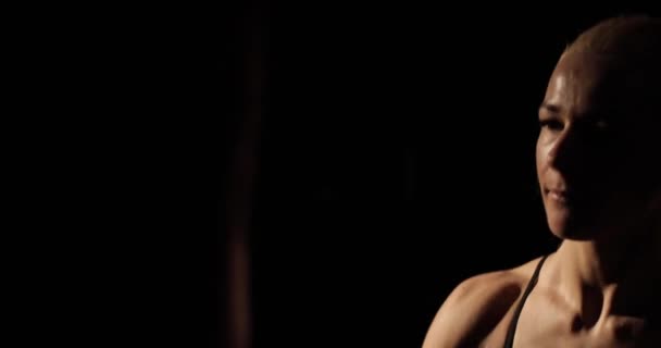 Close-up side lit materiał filmowy zdeterminowanej blondynki bokser agresywnie uderza w worek bokserski podczas treningu. — Wideo stockowe