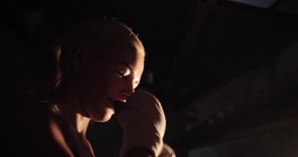 Primo piano lato illuminato filmato di una determinata bionda pugile femminile che lancia colpi durante l'allenamento. — Video Stock