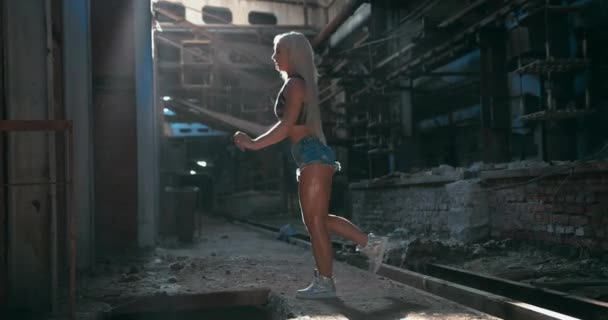 Attraktiv kaukasisk fitness modell gör benet swing och främre arm stretching motion i fabriken bakgrund — Stockvideo