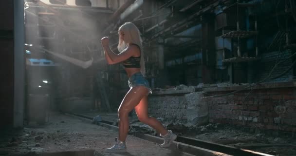 Pełne ujęcie atrakcyjnej kaukaskiej modelki fitness wykonującej uderzenie do przodu w fabrycznym tle — Wideo stockowe