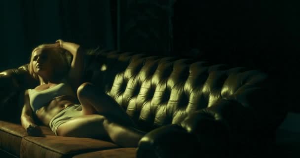 Sexy blondýny žena ležící na pohovce a svůdný dotýkat se jejích vlasů v tmavé místnosti.