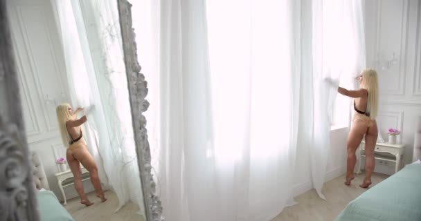 Mooie jonge vrouw met Sexy Fit lichaam Opening gordijnen In haar slaapkamer In de ochtend. Meisje permanent in de buurt van venster thuis. — Stockvideo