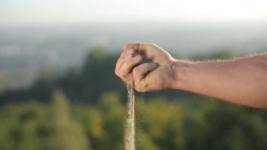 Erkek yumruğu. Yumruğunda kum var. Erkeklerin parmakları arasındaki kum akıntıları. Ufkun ve doğanın arkasında
