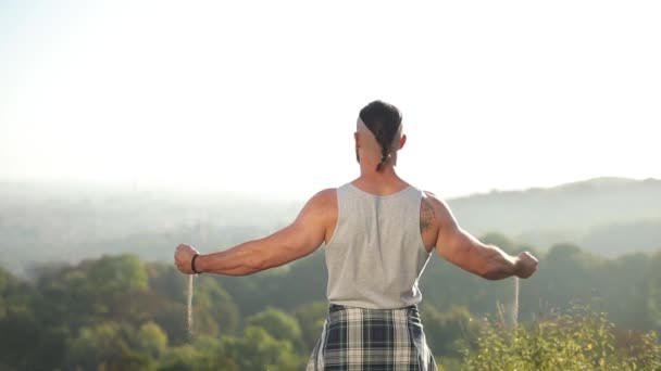 Un homme musclé se tient sur le bord devant le gouffre des mains, il verse du sable. l'homme se sent fort et libre. vue arrière — Video