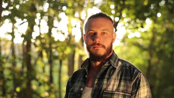 Close-up portret van aantrekkelijke man met baard, terug in het bos tussen bomen stralende zon — Stockvideo