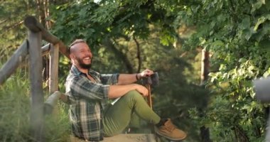 Basit giysiler içinde neşeli, mutlu, sakallı bir adam yerde oturuyor. Adam mutlu hissediyor. Adam neşeyle gülüyor.