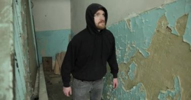 Siyah ışıklı ve gri kotlu sakallı bir adam merdivenlerden çıkıp harap olmuş bir eve gidiyor. Genç adam yıkılmış duvarlara bakıyor.