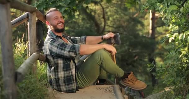 Człowiek w naturze czuje się szczęśliwy. młody człowiek siedzi w pobliżu drewnianego mostu w lesie lub parku. — Wideo stockowe