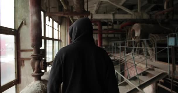 リアビューだ。黒いフードの服を着た男が放棄された工場の部屋を見て回り — ストック動画