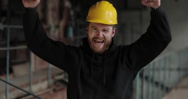 Très joyeux jeune homme à la barbe rouge se sent joyeux et heureux. le maître au casque jaune lève joyeusement les mains. émotion heureuse. — Video