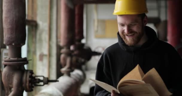 Joyful tovární dělník jde s dokumenty v rukou a usmívá se. muž v tmavých šatech, žlutá helma a papíry v rukou. — Stock video