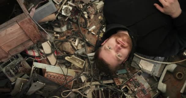 Mirada espeluznante del hombre. hombre con barba roja acostado en un montón de chatarra de radio, cables, chips, electrónica rota — Vídeos de Stock