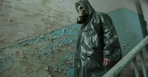 En man i overall och en gasmask med en behållare i handen går nerför trappan. Nästan förstört rum, nödtrappa, trasiga väggar — Stockvideo