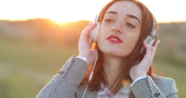 Yaşam tarzı konsepti - Neşeli kızıl saçlı kızıl saçlı kızın portresi kameraya gülümseyen kulaklıklarla müzik dinlemekten zevk alır. Doğa geçmişi. Çilli kız yüzü