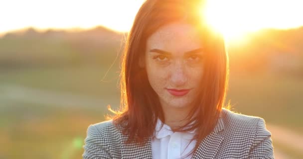 Retrato de cerca de una chica pelirroja con pecas en la cara en traje de negocios. detrás de la chica una hermosa puesta de sol — Vídeos de Stock